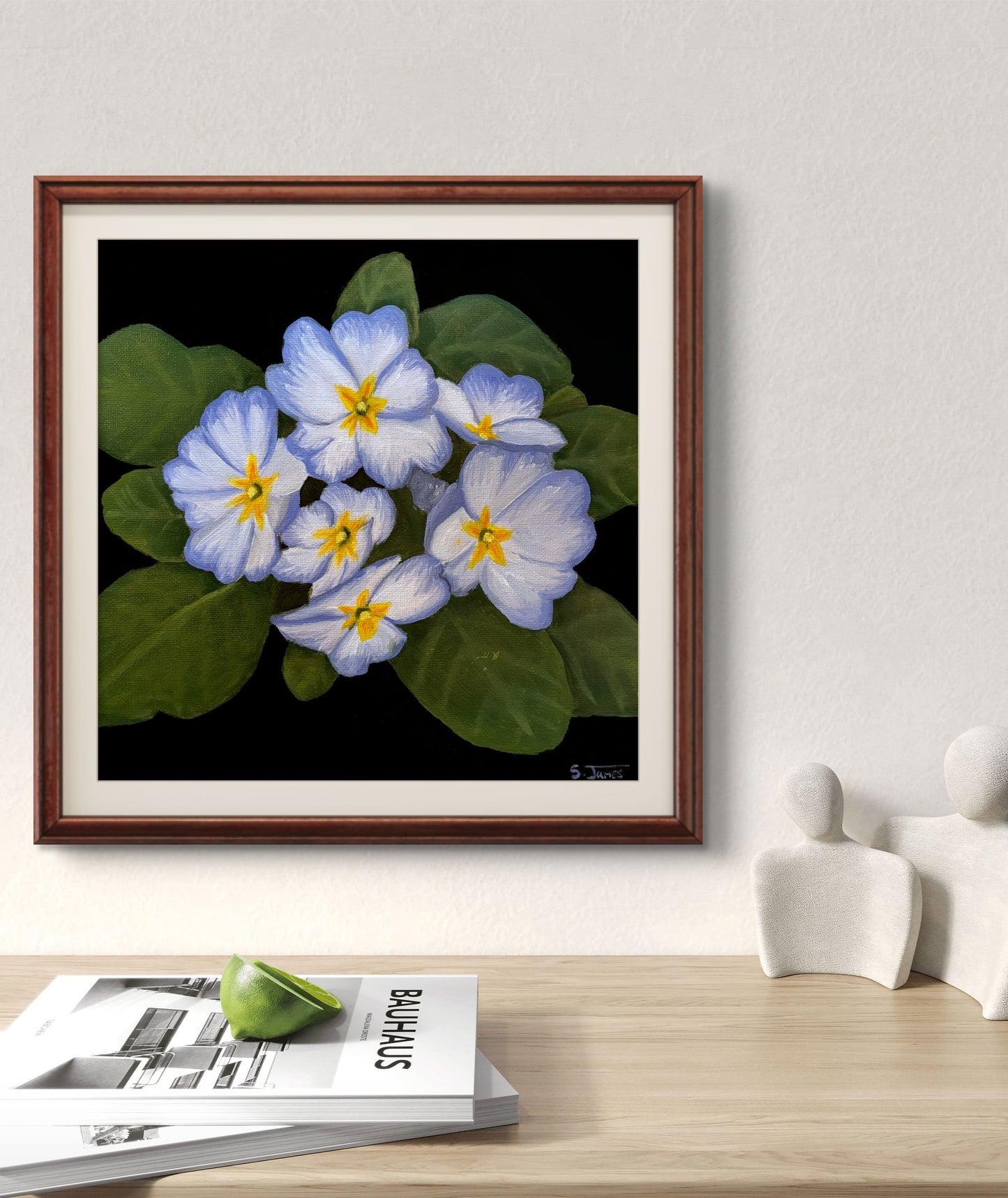 Framed artwork of blue and yellow flowers on a wall above a wooden surface with magazines and decorative items.